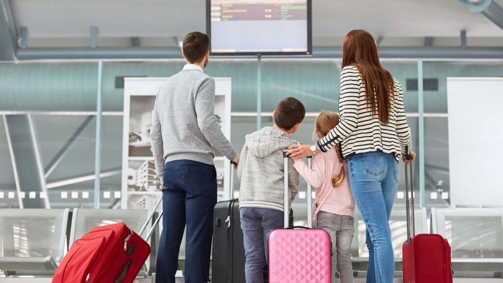 Famille à l’aéroport avec valises regardant l’écran des vols – préparation et organisation du voyage en Colombie.